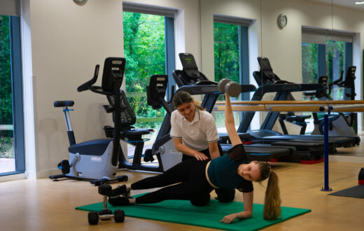 Women lifting a very heavy dumbbell whilst a physiotherapist assesses