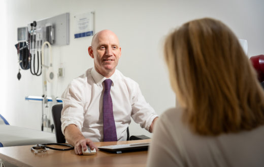 A private GP speaking with a patient behind a desk.