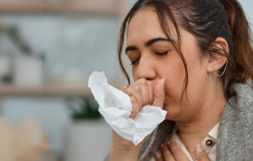 A young woman holds a tissue to her mouth while coughing, demonstrating a typical reaction to respiratory discomfort.