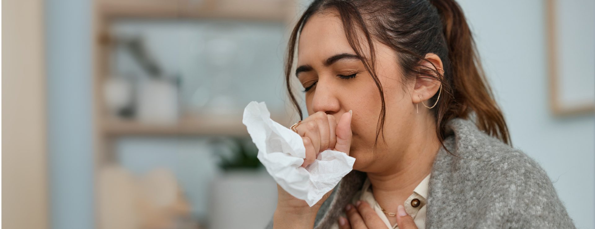 A young woman holds a tissue to her mouth while coughing, demonstrating a typical reaction to respiratory discomfort.