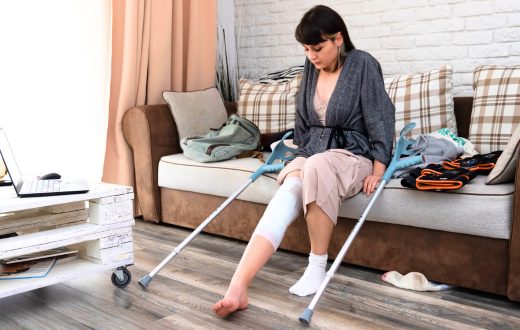 A woman with crutches sits comfortably on a sofa, recovering from knee replacement surgery