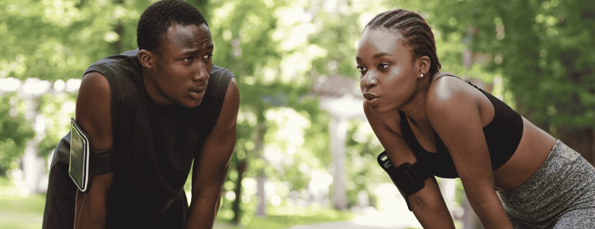 wo runners outdoors, a man supporting a woman who is out of breath after exercise
